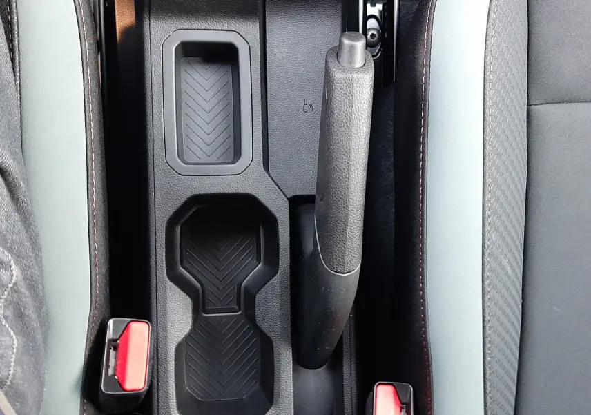 Gros plan sur la console centrale noire avec frein à main et porte-gobelets du Dacia Duster 1.6 Hybrid 140ch Sandstone.
