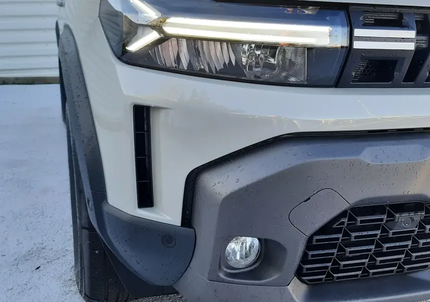Gros plan sur l'avant gauche du Dacia Duster 2025 Sandstone, mettant en valeur ses phares LED et sa calandre robuste.
