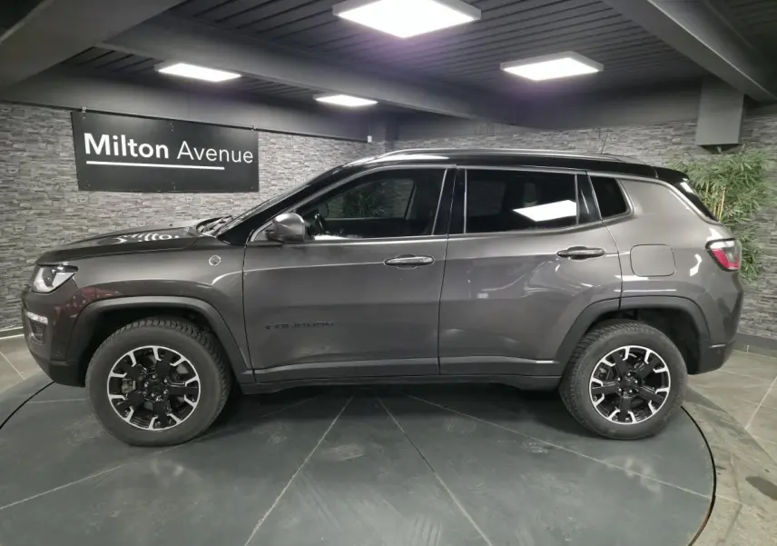 Profil côté gauche d'un Jeep Compass gris foncé avec jantes alliage noires et toit noir en showroom.