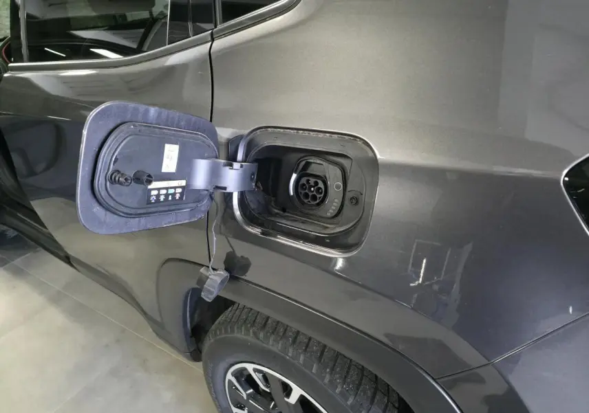 Prise de recharge ouverte côté gauche sur Jeep Compass gris foncé hybride rechargeable, avec jante alliage visible.