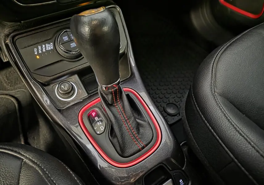 Gros plan sur la console centrale du Jeep Compass 2020 avec levier de vitesses cuir noir et surpiqûres rouges.