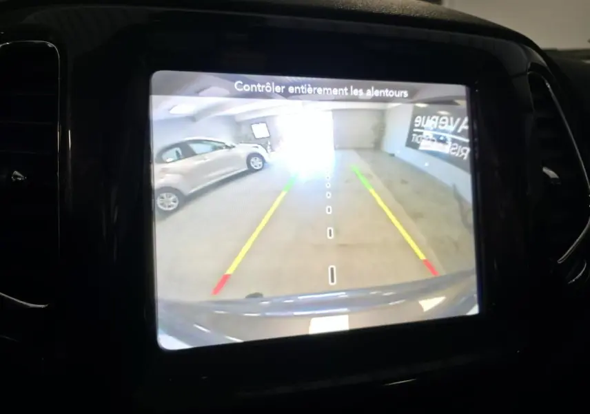 Écran de caméra de recul affichant l'arrière du Jeep Compass gris foncé dans un garage lumineux.