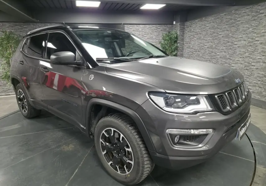 Jeep Compass gris foncé en vue 3/4 avant droit, avec jantes alliage noires et toit noir en intérieur showroom.