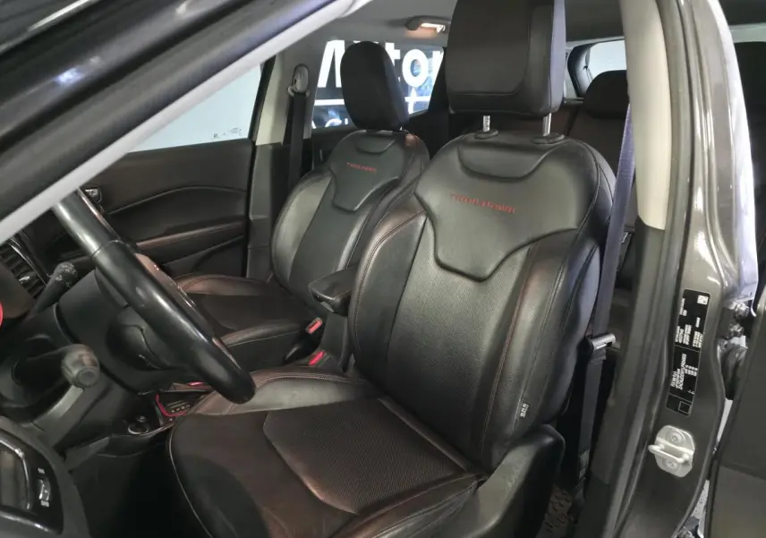 Vue intérieure côté conducteur du Jeep Compass gris foncé, sièges cuir noirs avec logo Trailhawk rouge brodé.