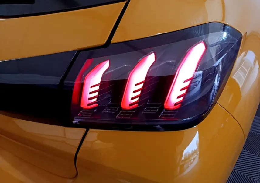 Gros plan sur le feu arrière droit allumé d’une Peugeot 208 jaune PureTech 2023, soulignant ses trois griffes lumineuses rouges.