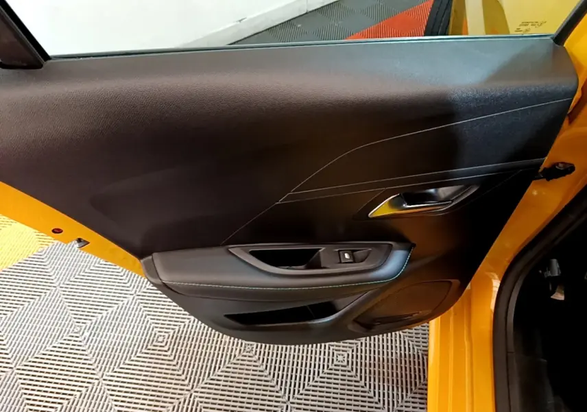 Vue rapprochée de la porte arrière gauche jaune d’une Peugeot 208 2023, avec poignée intérieure et commande de vitre noire.