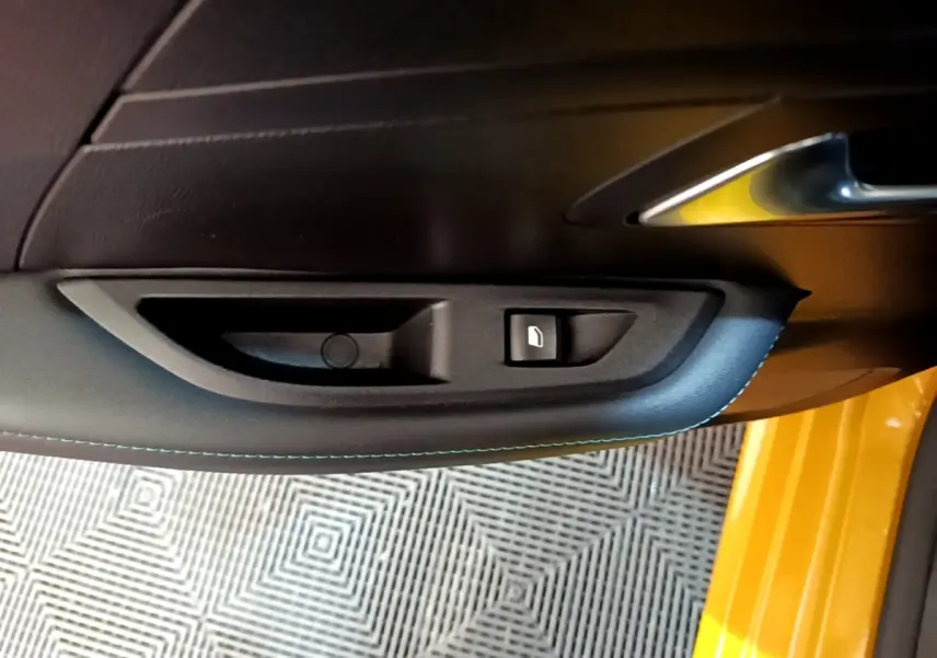 Poignée intérieure côté gauche de porte PEUGEOT 208 jaune 2023 avec bouton de verrouillage et surpiqûres bleues.