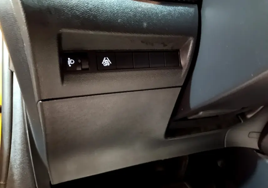 Détail intérieur côté gauche de la Peugeot 208 jaune 2023, avec commandes d'éclairage et d'aide à la conduite.