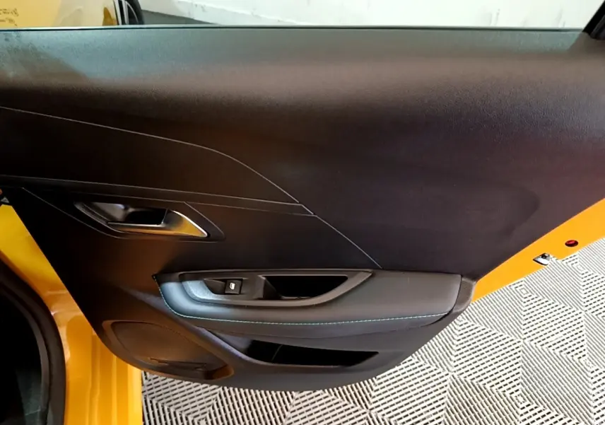 Vue rapprochée de la porte intérieure côté gauche d'une Peugeot 208 jaune avec garniture noire et surpiqûres bleues.
