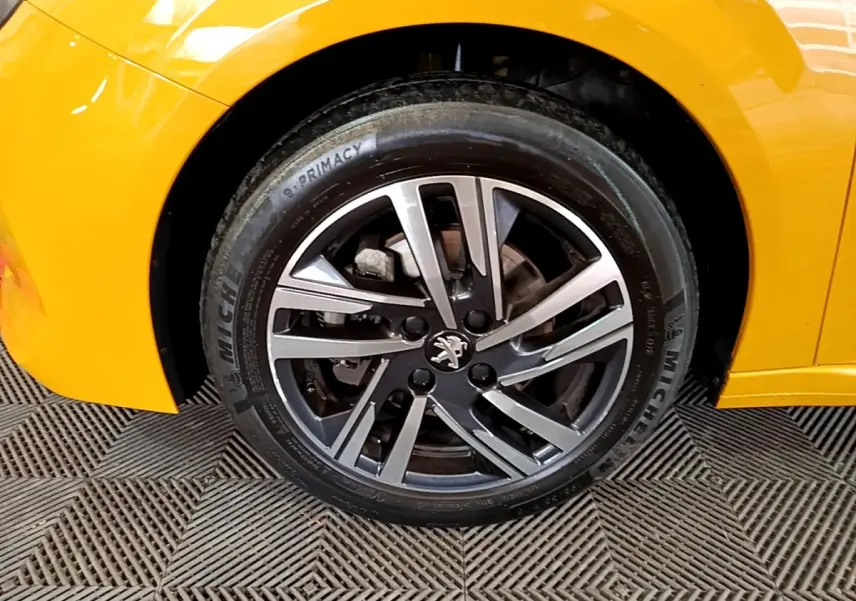 Gros plan sur la roue avant gauche d’une Peugeot 208 jaune 2023 avec jante alliage et logo lion au centre.