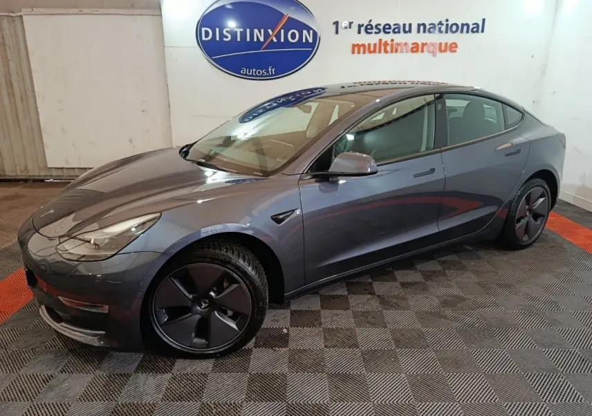 Tesla Model 3 Grande Autonomie gris foncé vue de côté droit en intérieur avec jantes noires et logo visible.