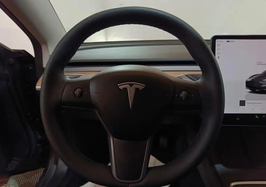 Vue rapprochée du volant noir de la Tesla Model 3 Grande Autonomie 2022 avec écran tactile central visible à droite.