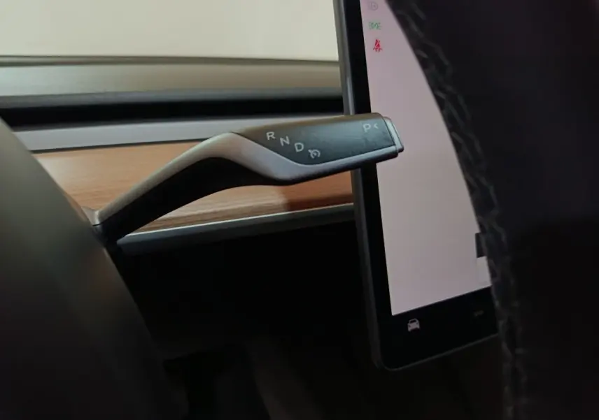 Gros plan sur le levier de vitesses noir et argenté à droite du volant dans l’habitacle gris foncé d’une Tesla Model 3 2022.
