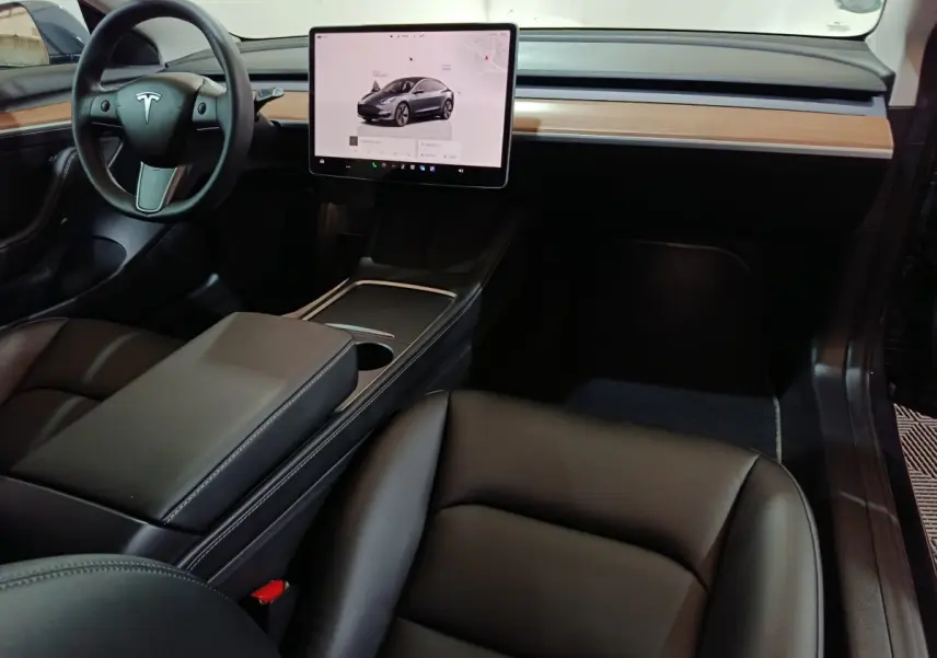 Intérieur avant de la Tesla Model 3 gris foncé, avec tableau de bord minimaliste et grand écran tactile central.