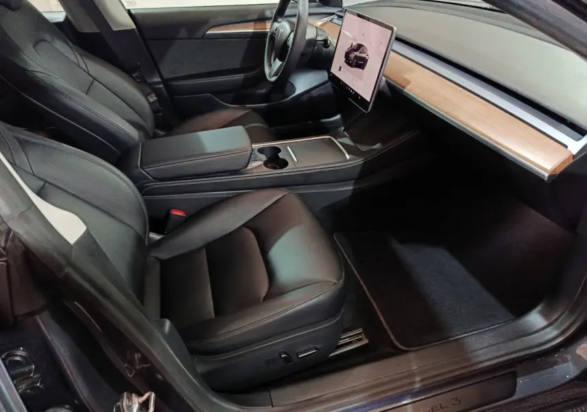Intérieur Tesla Model 3 Grande Autonomie 2022 vu côté passager, sièges noirs et tableau de bord bois clair avec écran tactile central.