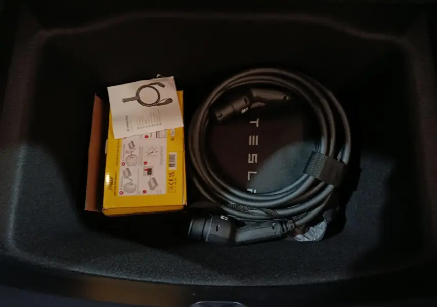 Vue intérieure du coffre d'une Tesla Model 3 gris foncé avec câble de charge et boîte jaune de rangement.