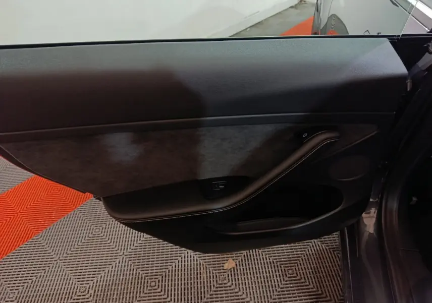 Gros plan sur la porte intérieure côté gauche d'une Tesla Model 3 gris foncé, avec garniture noire et bouton de vitre.
