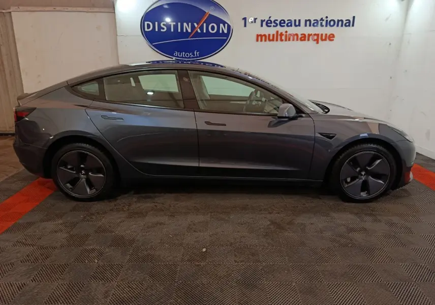 Profil droit d'une Tesla Model 3 Grande Autonomie gris foncé, avec jantes aérodynamiques et poignées affleurantes.