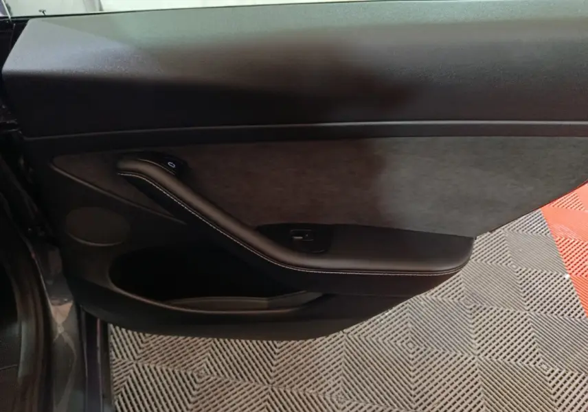 Vue intérieure du panneau de porte côté conducteur gris foncé de la Tesla Model 3 Grande Autonomie 2022 avec accoudoir et commande de vitre.