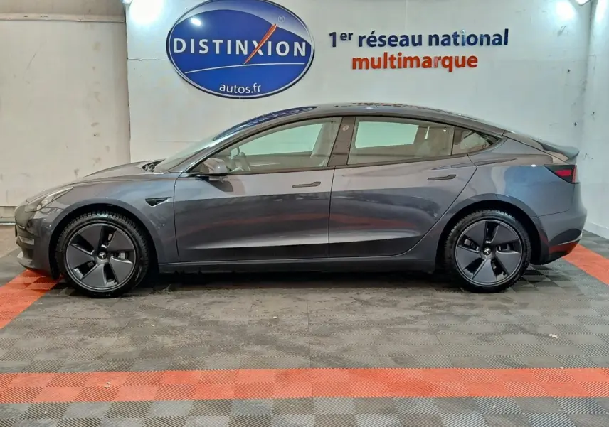 Vue latérale droite d'une Tesla Model 3 Grande Autonomie gris foncé, avec jantes aérodynamiques et logo distinctif.