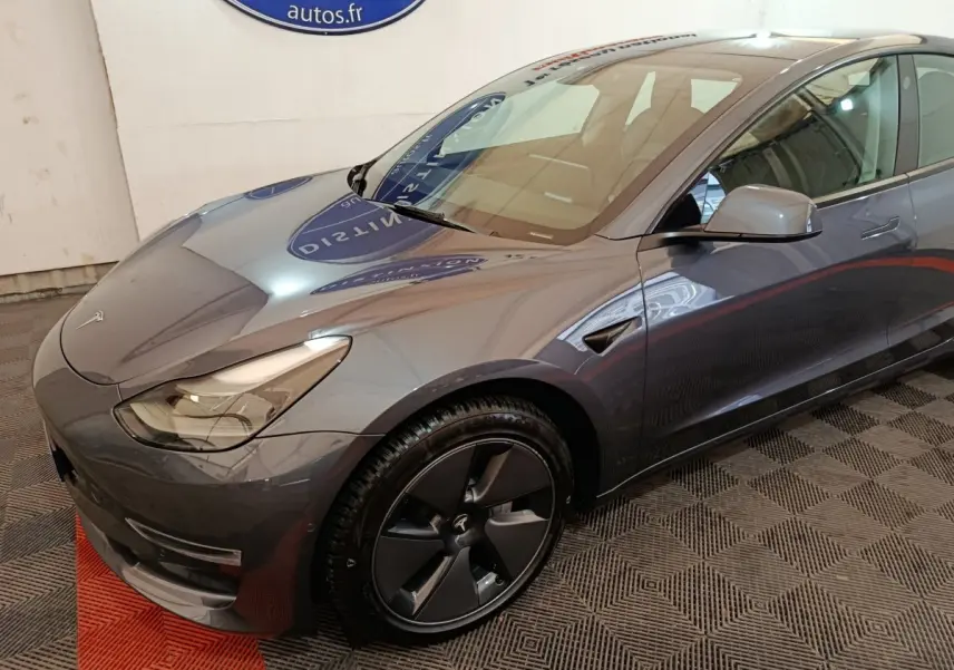 Vue 3/4 avant droit d'une Tesla Model 3 Grande Autonomie gris foncé avec jantes noires et phares LED.