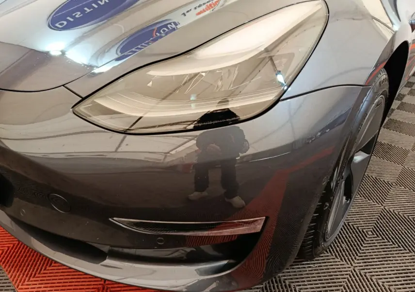 Gros plan sur l'avant droit gris foncé d'une Tesla Model 3 2022, mettant en valeur le phare LED et la jante noire.
