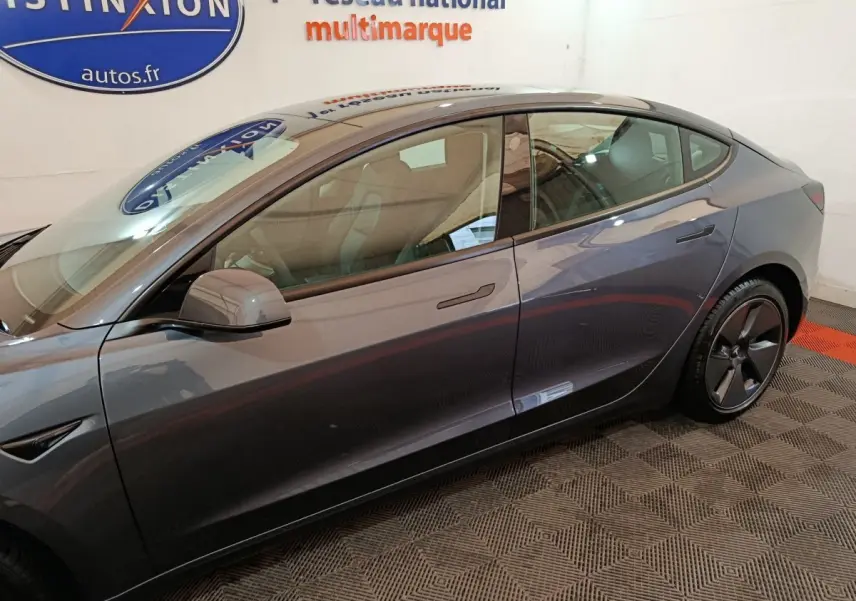 Profil côté gauche d'une Tesla Model 3 Grande Autonomie gris foncé, avec poignées affleurantes et jantes aérodynamiques.