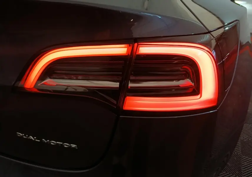 Gros plan sur le feu arrière droit rouge allumé d’une Tesla Model 3 Grande Autonomie gris foncé.