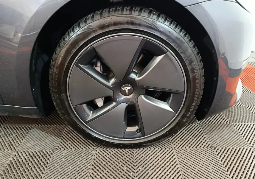 Gros plan sur la roue avant droite d’une Tesla Model 3 gris foncé avec jante aérodynamique.
