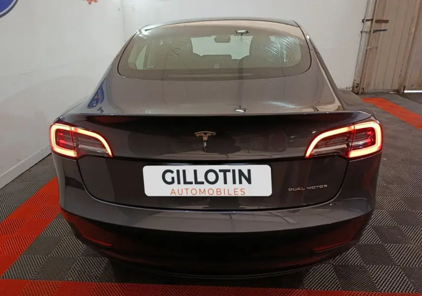 Vue arrière d'une Tesla Model 3 Grande Autonomie gris foncé avec feux LED allumés dans un garage.
