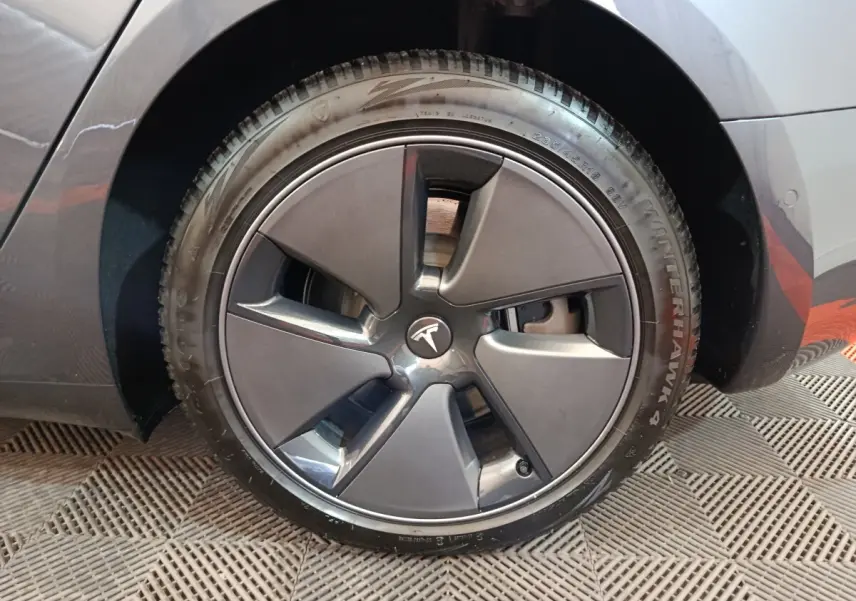 Vue rapprochée de la roue arrière droite d'une Tesla Model 3 gris foncé, montrant le passage de roue et le pneu Winterhawk 4.
