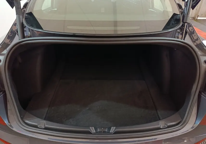 Coffre ouvert vu de l'arrière d'une Tesla Model 3 gris foncé, montrant l'espace de rangement vide.