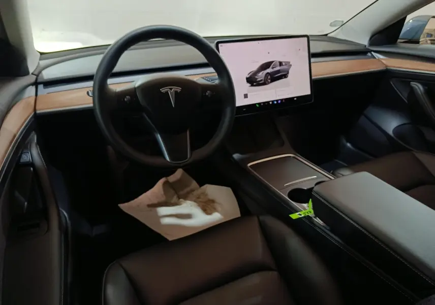 Intérieur noir de Tesla Model 3 2022, vue du poste de conduite avec écran tactile central et tableau de bord bois.