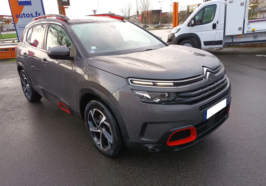 Citroën C5 Aircross gris platinium en 3/4 avant gauche avec détails rouges contrastants sur pare-chocs et bas de caisse.