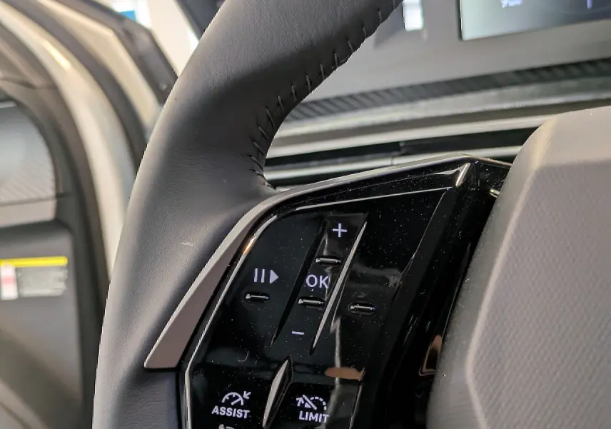 Gros plan sur les commandes au volant côté gauche du Peugeot 5008 blanc Okenite, avec écran digital en arrière-plan.