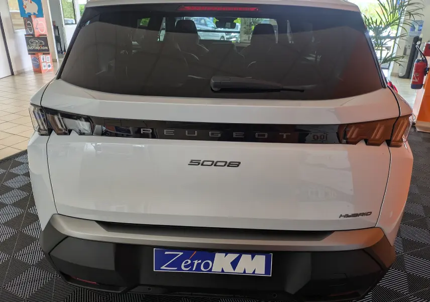 Vue arrière d’un Peugeot 5008 blanc Okenite hybride, avec feux arrière en bandeau noir et logo PEUGEOT lumineux.