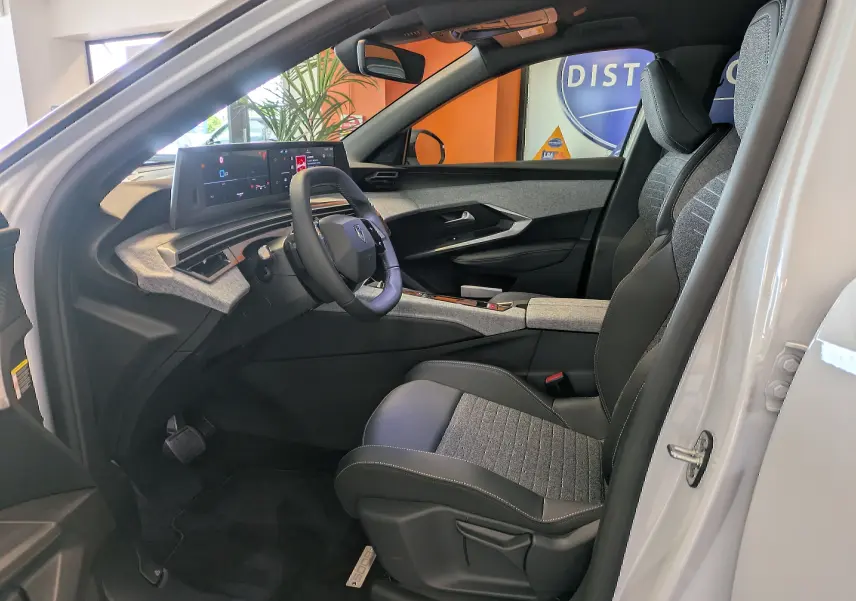 Vue intérieure côté conducteur du Peugeot 5008 blanc Okenite 2025, avec tableau de bord numérique et sièges bi-matière gris et noir.
