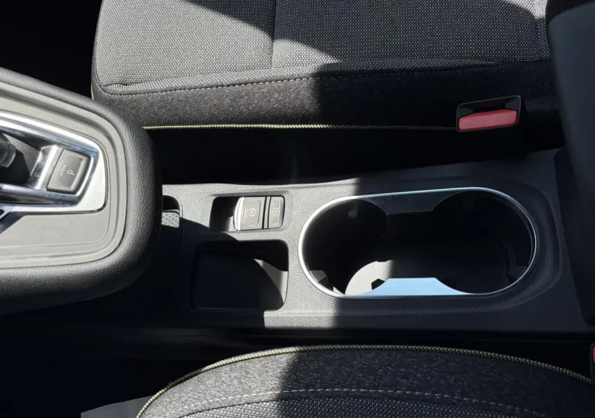 Gros plan sur la console centrale noire du Renault Captur 2025 avec porte-gobelets et commandes de frein à main électrique.
