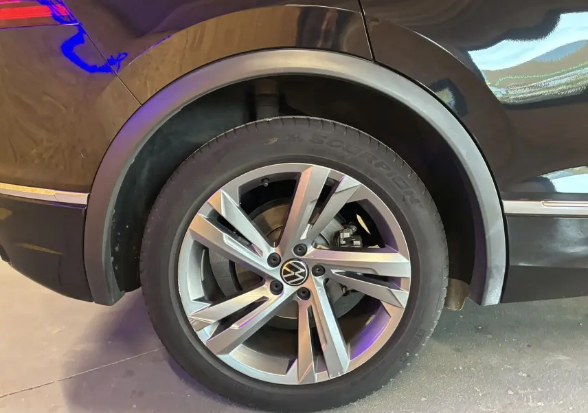 Gros plan sur la roue arrière droite du Volkswagen Tiguan noir avec jante alu et logo VW au centre.