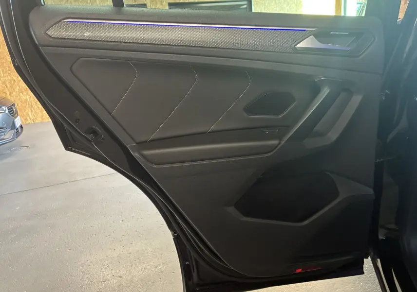 Vue intérieure de la porte arrière gauche noire du Volkswagen Tiguan 2.0 TDI 150 DSG7 R-Line avec garniture en tissu et cuir.