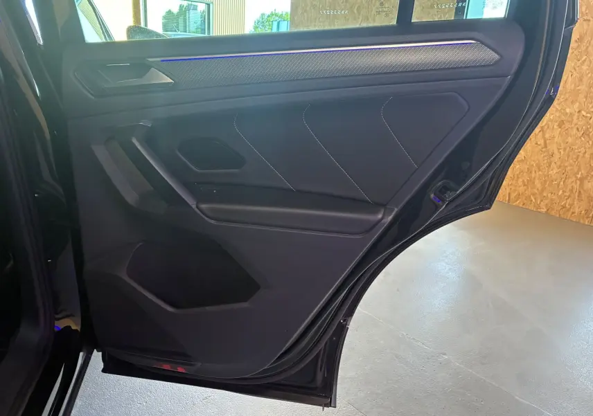 Porte arrière côté droit ouverte du Volkswagen Tiguan noir, intérieur tissu noir avec surpiqûres blanches et éclairage d'ambiance bleu.