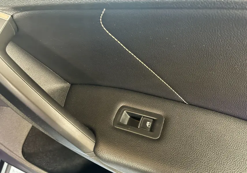 Détail de la commande de lève-vitre sur la porte intérieure noire avec surpiqûres blanches du Volkswagen Tiguan 2022.
