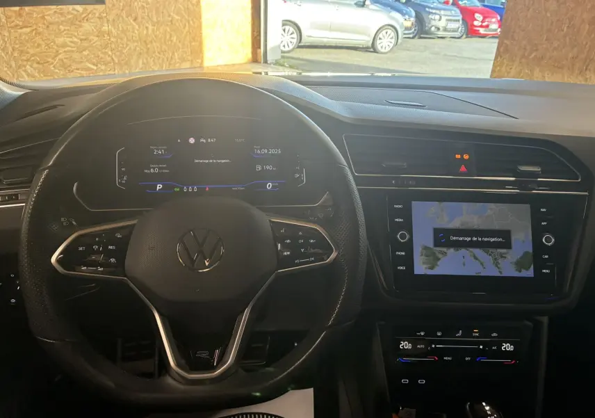 Vue intérieure du tableau de bord du Volkswagen Tiguan noir, avec volant multifonctions et écran tactile de navigation en démarrage.