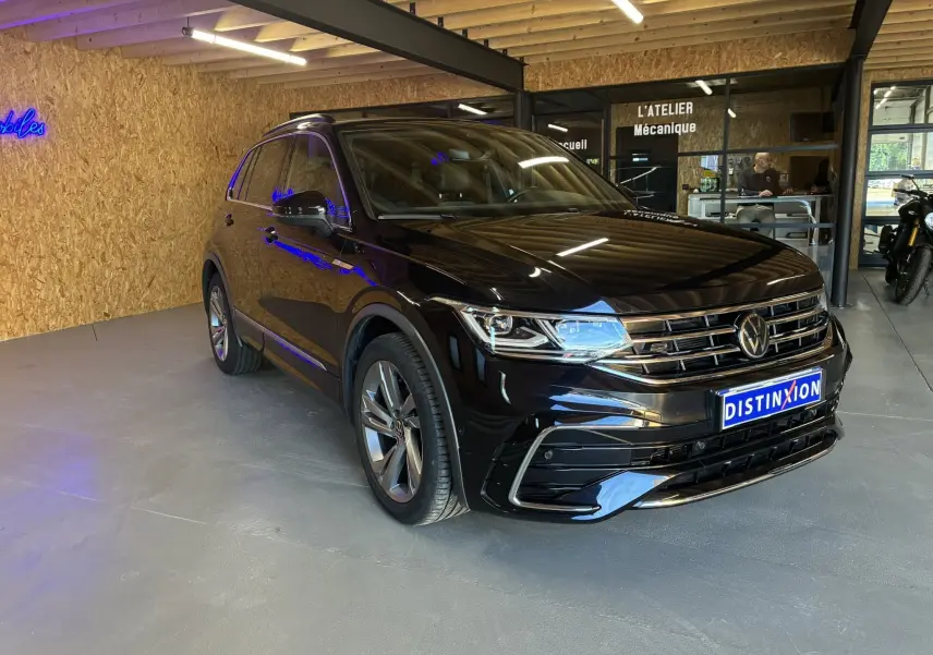 Volkswagen Tiguan noir en 3/4 avant droit, avec jantes alu et calandre chromée, stationné en intérieur d'atelier.