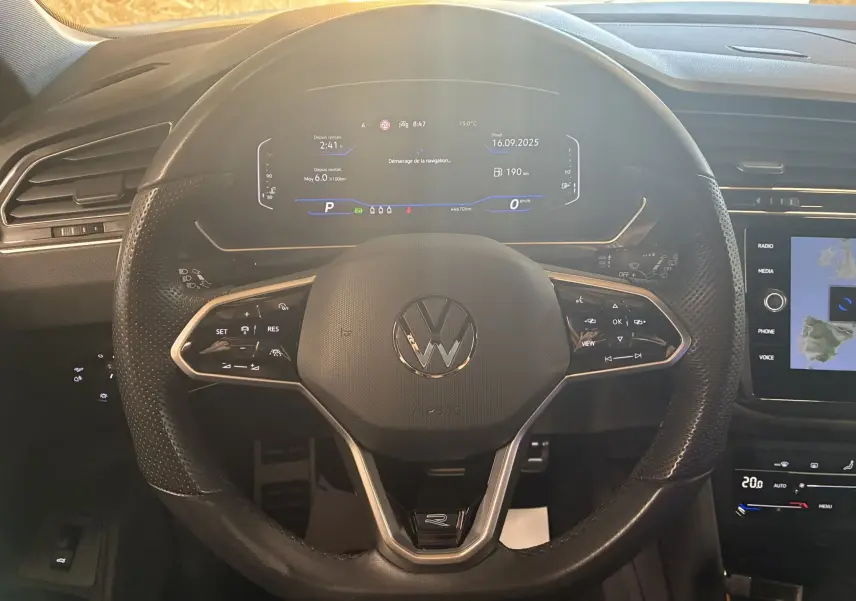 Vue rapprochée du volant cuir multifonctions noir du Volkswagen Tiguan 2.0 TDI R-Line avec tableau de bord digital allumé.