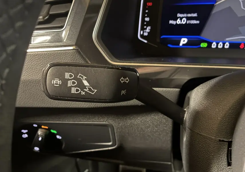 Gros plan sur le commodo gauche du volant d'un Volkswagen Tiguan noir 2022, avec tableau de bord numérique en arrière-plan.