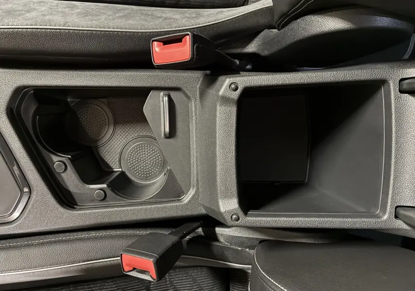 Vue plongeante sur la console centrale noire du Volkswagen Tiguan 2.0 TDI, avec porte-gobelets et accoudoir ouvert.
