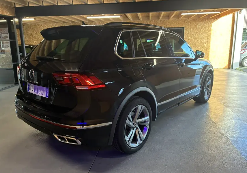 Volkswagen Tiguan noir en 3/4 arrière droit, avec jantes alu et double sortie d’échappement chromée.