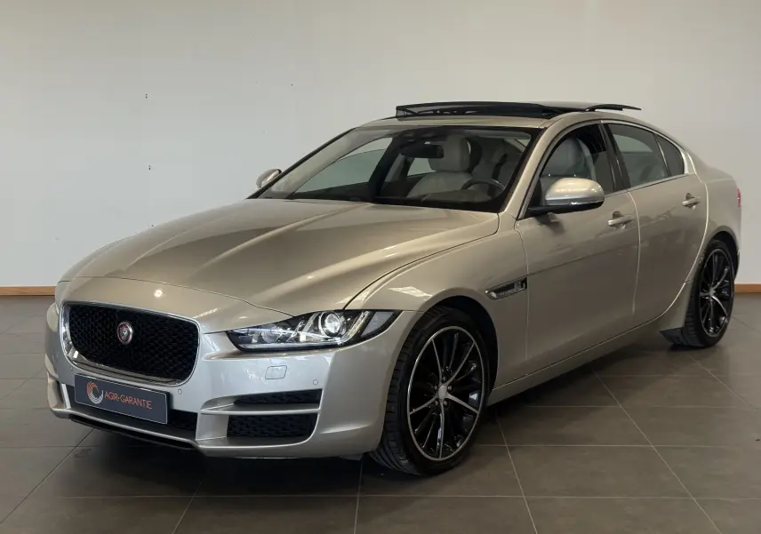Jaguar XE beige vue 3/4 avant droit avec toit ouvrant et jantes noires en intérieur showroom.