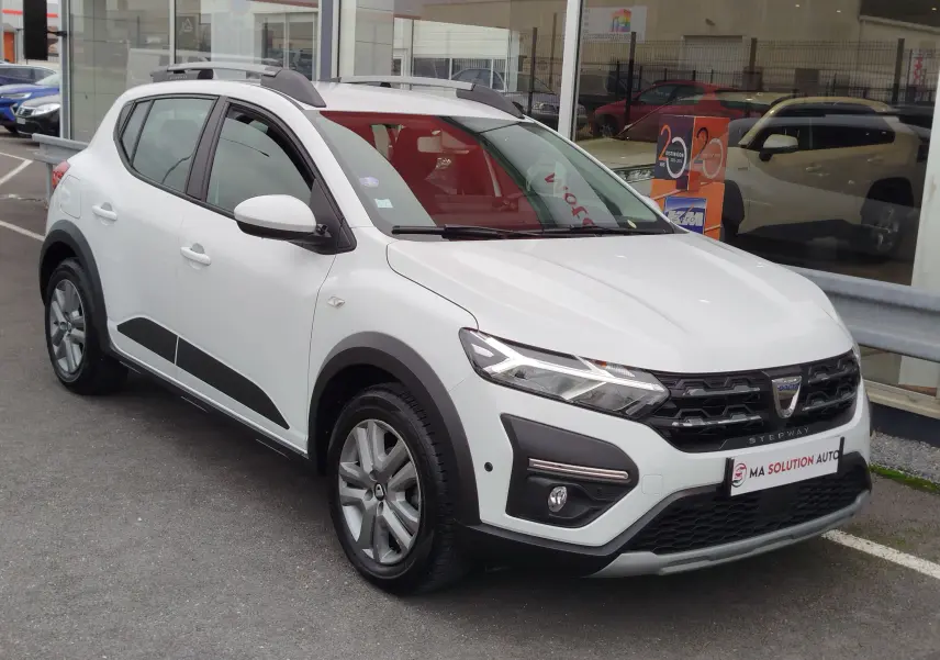 Vue 3/4 avant d'une Dacia Sandero Stepway blanche glacier avec détails noirs et barres de toit grises.